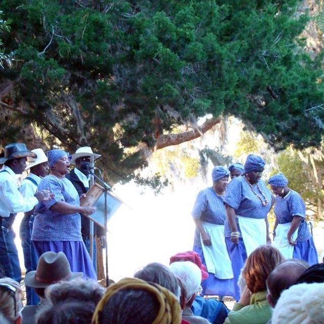 Ringshouters with audience; women dancing and woman singing with men playing intruments and clapping